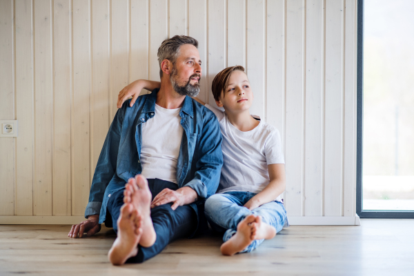 Mature father with small son sitting indoors ont the floor, talking.