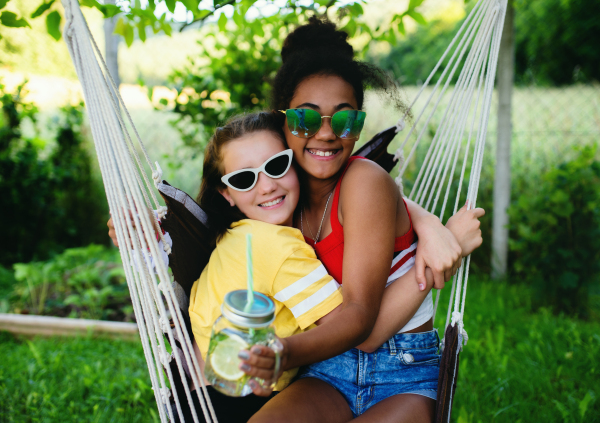 Front view of cheerful young teenager girls friends outdoors in garden, hugging.