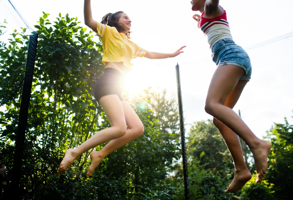 Low angle view of cheerful young teenager girls friends outdoors in garden, jumping on trampoline.