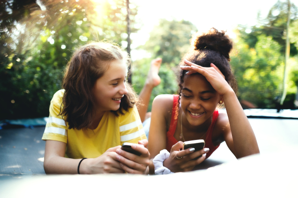 Front view of cheerful young teenager girls friends outdoors in garden, using smartphone.