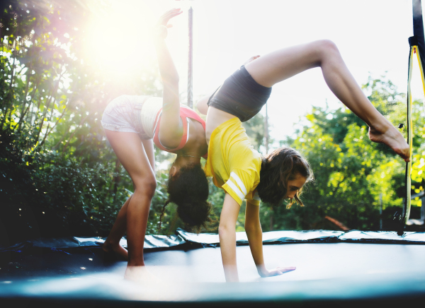 Front view of cheerful young teenager girls friends outdoors in garden, doing exercise on trampoline.