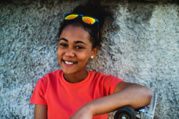 Side view of young teenager girl sitting outdoors in city, leaning on concrete wall.