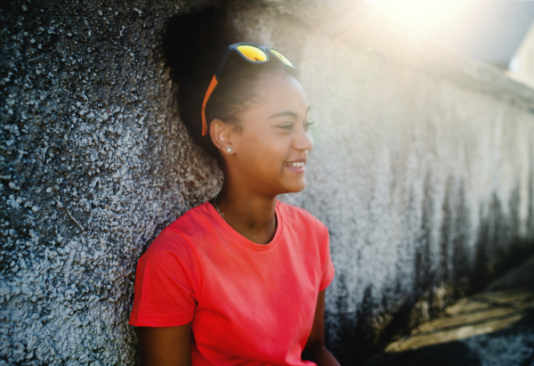 Side view of young teenager girl sitting outdoors in city, leaning on concrete wall.