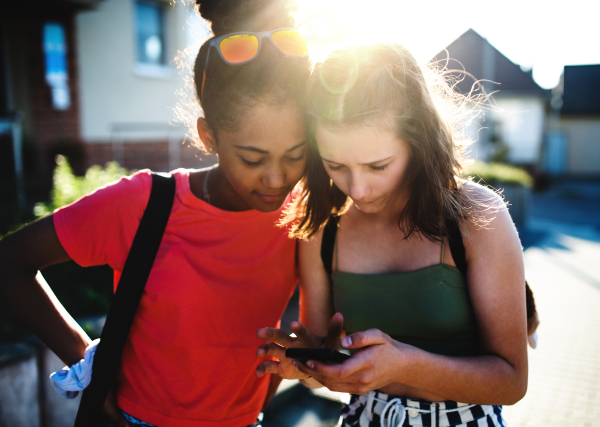 Front view of teenager girls friends outdoors in city, using sartphone.