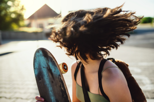 Front view of unrecognizable teenager girl with skateboard outdoors in city, having fun.