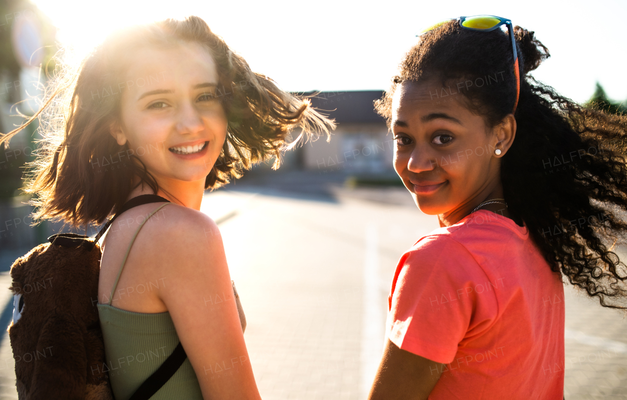 Cheerful teenager girls friends walking outdoors in city, looking at camera.