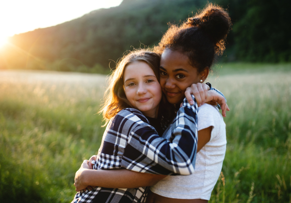 Front view of cheerful young teenager girls friends outdoors in nature, hugging.