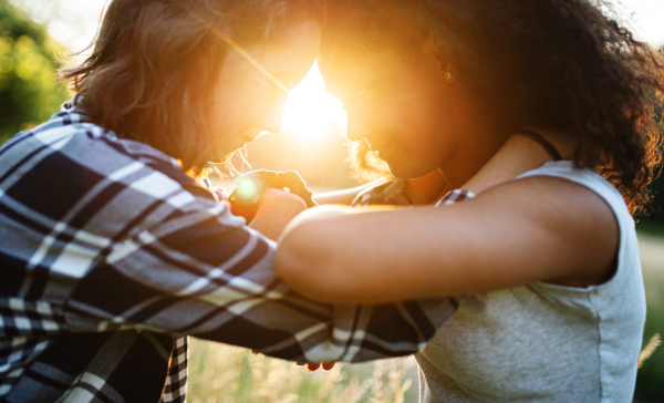 Side view of happy young teenager girls friends outdoors in nature at sunset, hugging.