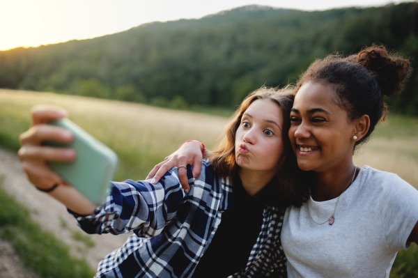 Front view of cheerful young teenager girls friends outdoors in nature, taking selfie with smartphone.