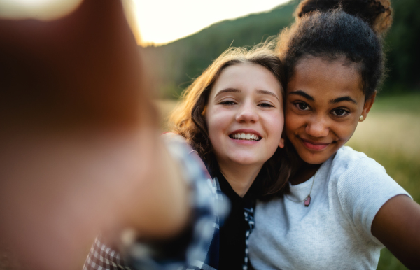 Front view of cheerful young teenager girls friends outdoors in nature, taking selfie with smartphone.