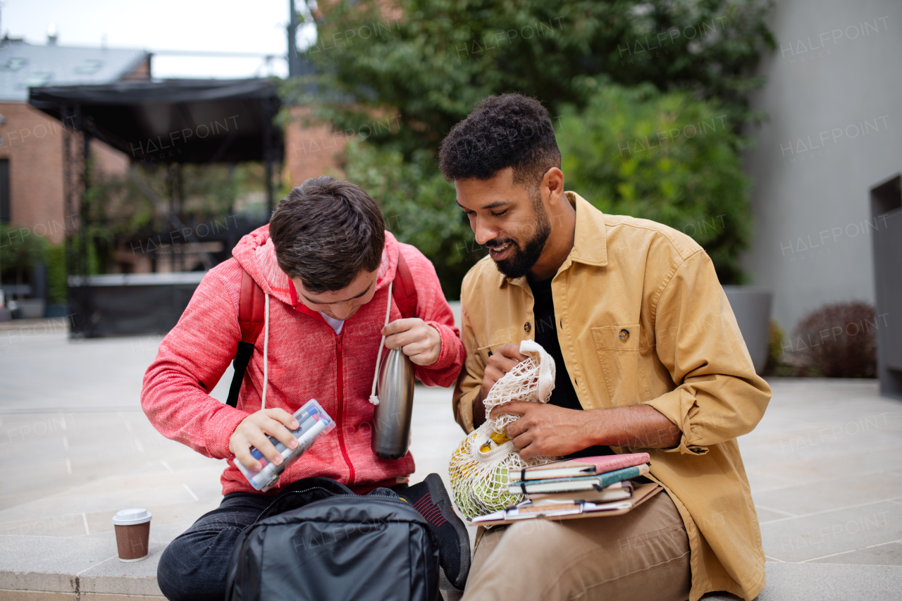 A young man student with Down syndrome and his mentoring friend sitting outdoors in campus area