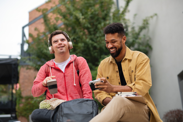 A young man student with Down syndrome and his mentoring friend sitting outdoors in campus area