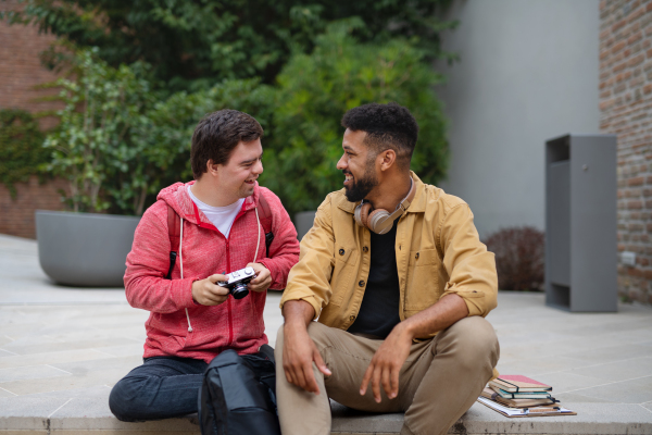 A happy young man with Down syndrome and mentoring friend sitting outdoors