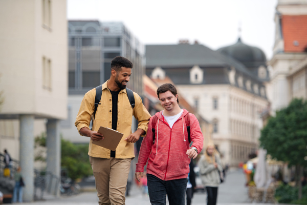 A young man with Down syndrome and his mentoring friend walking and talking outdoors