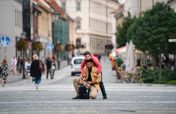 A young man with Down syndrome and mentoring friend embracing and looking at camera outdoors in town