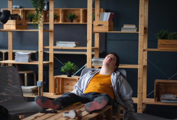 A young tired man with Down syndrome sitting indoors at school, taking break