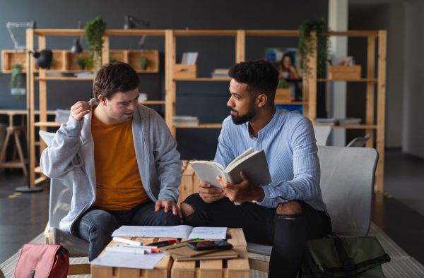 A young happy man with Down syndrome and his tutor studying indoors at school.