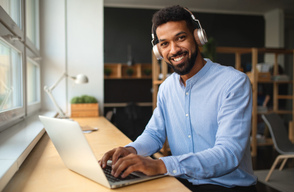 A young African-american teacher with headset and laptop indoors in staffroom looking at camera.