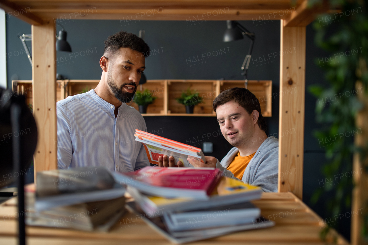 A young happy man with Down syndrome and his tutor indoors at staffroom.