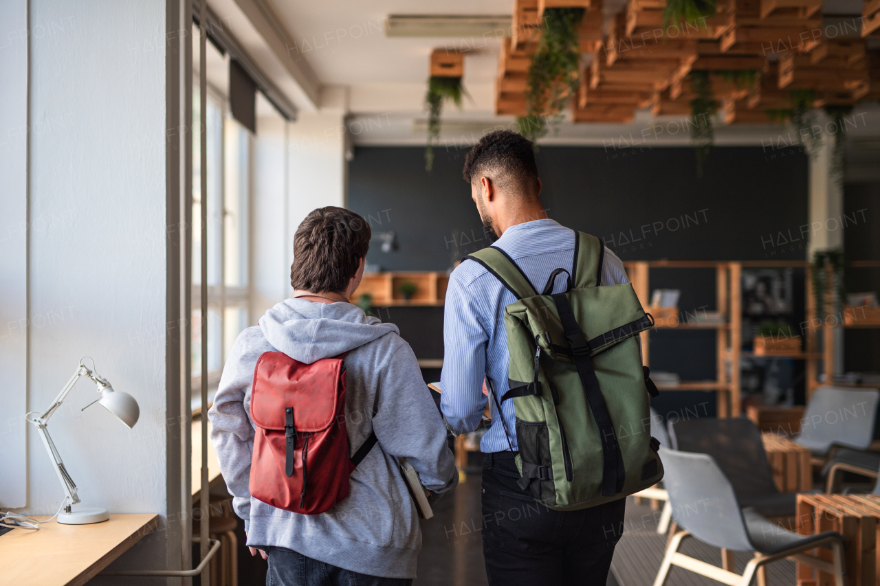 A rear view of young man with Down syndrome and his tutor indoors at school