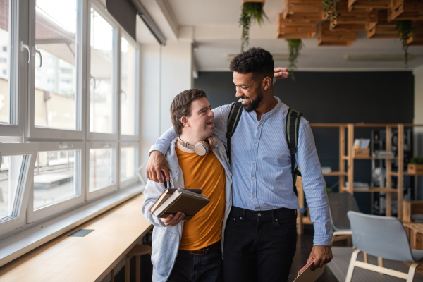 A young man with Down syndrome and his tutor with arms around looking at each other indoors at school