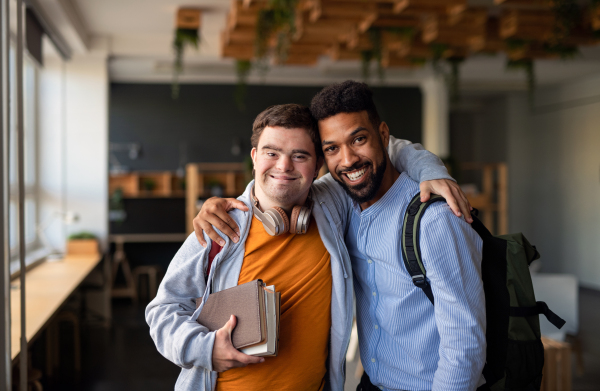 Happy young man with Down syndrome and his tutor with arms around looking at camera indoors at school