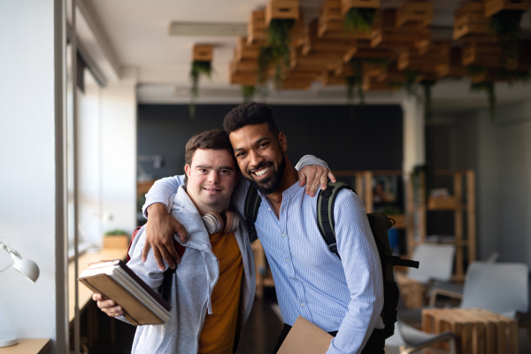 Happy young man with Down syndrome and his tutor with arms around looking at camera indoors at school