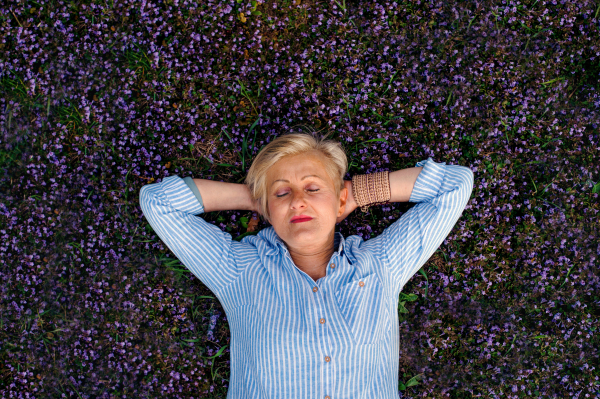 Top view of senior woman with closed eyes lying on flowers on grass on meadow.