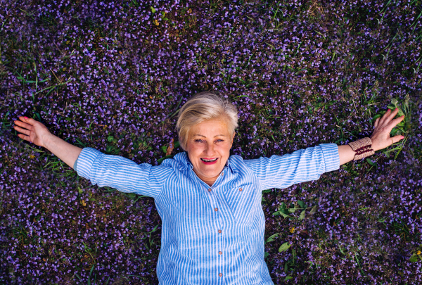 Top view of senior woman lying on flowers on grass on meadow.