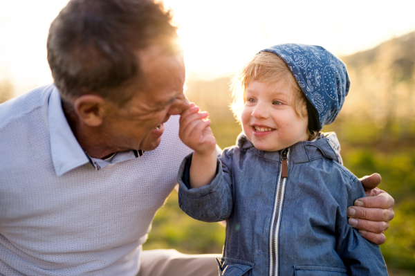 Senior grandfather with toddler grandson standing in nature in spring, having fun.