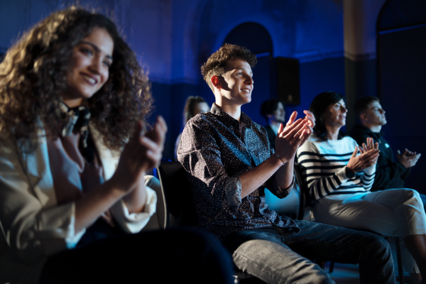 A group of people clapping while listening to presentation at conference.