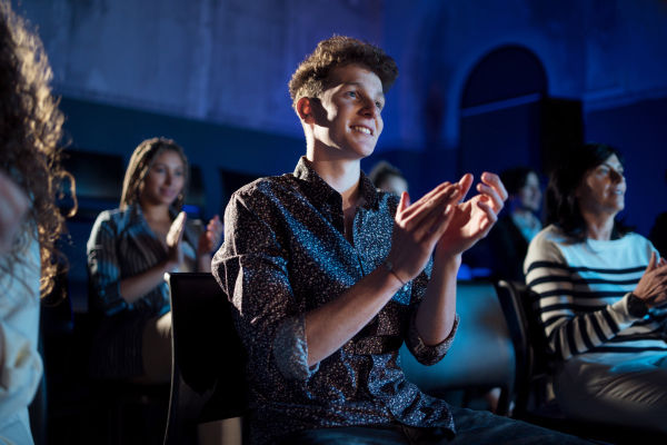 A group of people clapping while listening to presentation at conference.