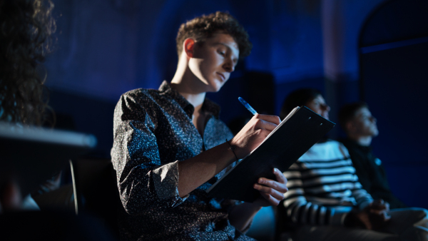 A young man making notes while listening to presentation at conference.