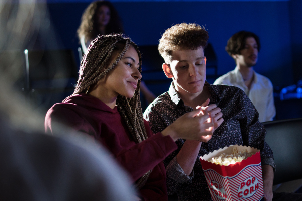 Cheerful young couple eating popcorn while watching movie in cinema.