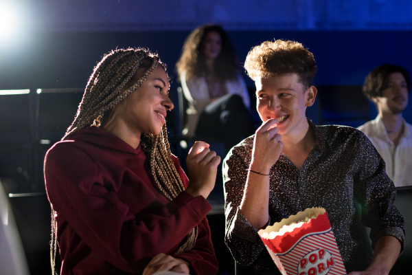 Cheerful young couple eating popcorn while watching movie in cinema, laughing.