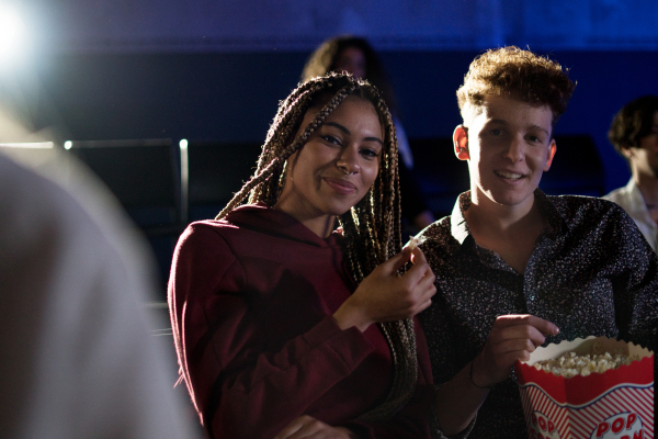 Cheerful young couple eating popcorn while watching movie in cinema, looking at camera.