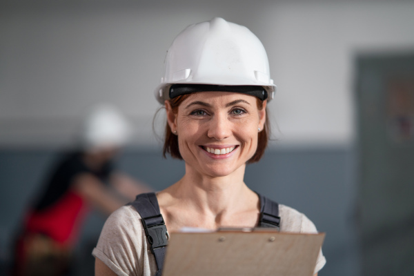 A low-angle view of worker with helmet indoors in factory looking at camera.