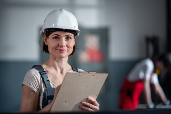 A low-angle view of worker with helmet indoors in factory holding clipboard.