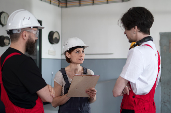 A group of workers with helmet indoors in factory, discussing issues.