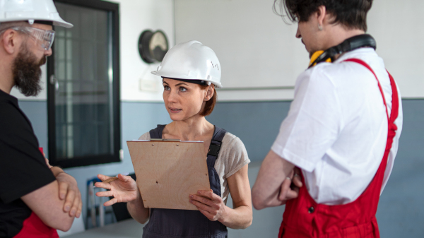 A group of workers with helmet indoors in factory, discussing issues.