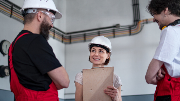 A group of workers with helmet indoors in factory, discussing issues.