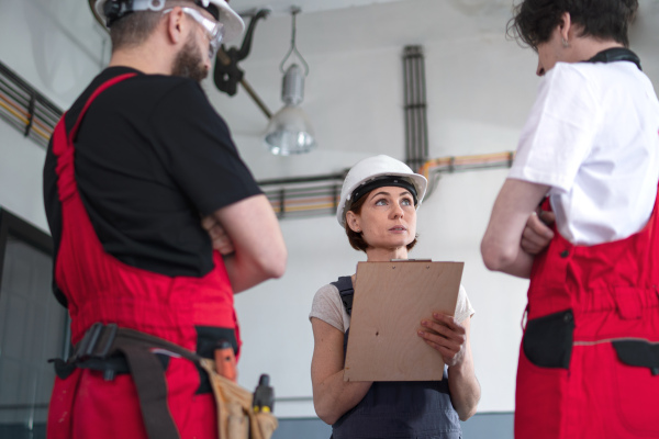 A group of workers with helmet indoors in factory, discussing issues.