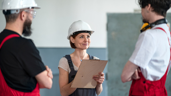 A group of workers with helmet indoors in factory, discussing issues.