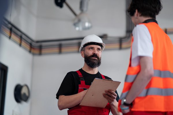 Portrait of men workers with helmet working indoors in factory, discussing issues.