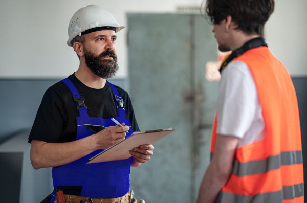 Portrait of men workers with helmet working indoors in factory, discussing issues.