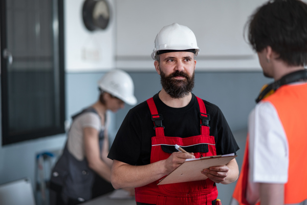 Portrait of men workers with helmet working indoors in factory, discussing issues.