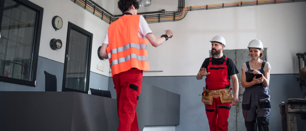 A group of workers with helmet indoors in factory, discussing issues.