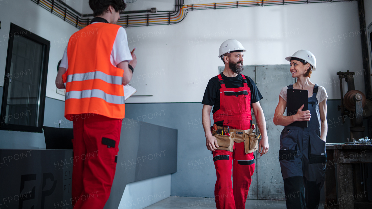 A group of workers with helmet indoors in factory, discussing issues.