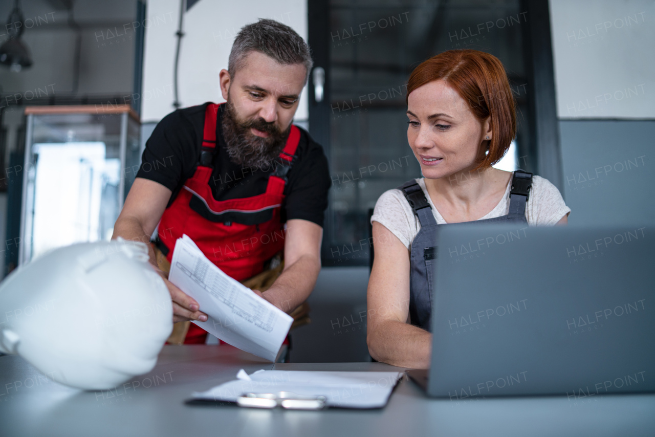 Group of workers or industry engineers with laptop indoors in factory, discussing issues at work.