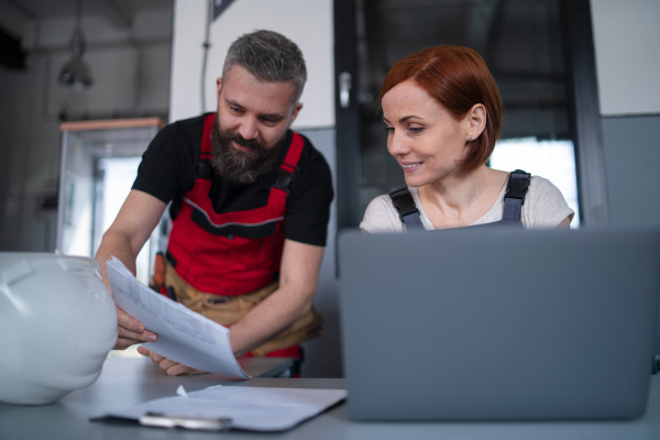 Mature man and woman workers or industry engineers with laptop indoors in factory, discussing issues.